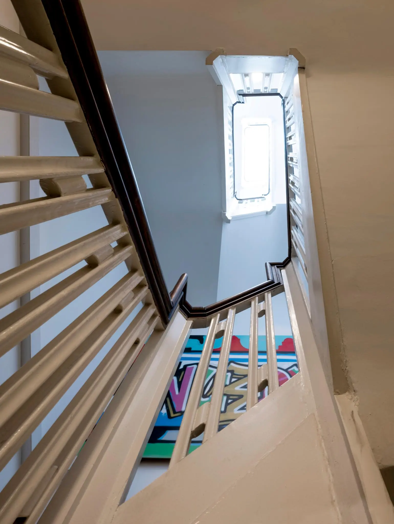 Trapopgang in een gebouw aan de Nieuwezijds Voorburgwal met zicht op een kunstwerk en een lichtinval van bovenaf.